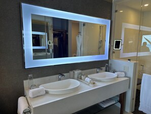 Un baño moderno con dos lavamanos, un espejo grande y una ducha con mampara de vidrio.