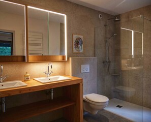 Une salle de bain moderne avec deux lavabos, des toilettes et une douche à parois de verre.