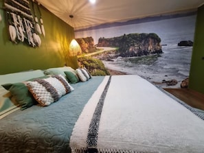 Un dormitorio con cama, almohadas y un mural costero.