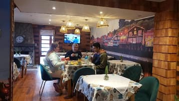 A restaurant with wooden walls, tables with patterned tablecloths, and hanging lights.