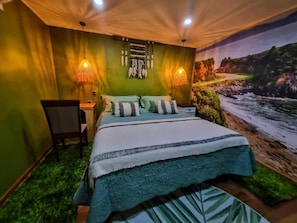 Un dormitorio con una cama, dos lámparas de pared, una silla y un mural de un paisaje costero.