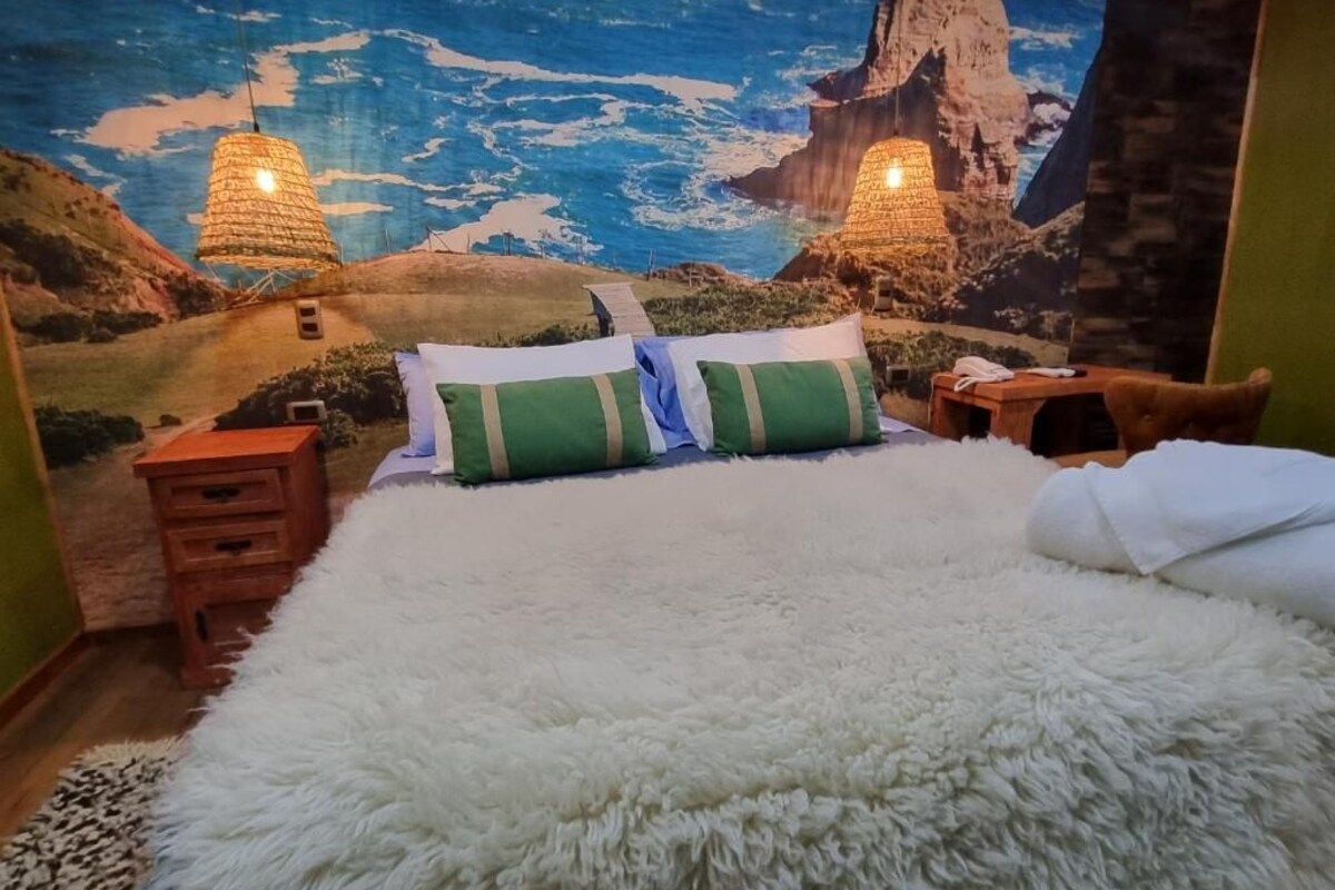 Un dormitorio con una cama grande, una mesita de noche de madera y un mural en la pared que representa un paisaje costero.