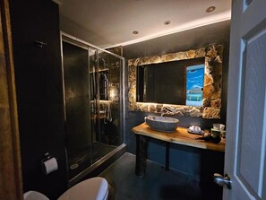 Un baño moderno con ducha envuelta en cristal, pared de detalles en piedra y tocador de madera con lavabo.