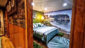 A bedroom with a bed, a wall mural of a beach, and a wooden floor.