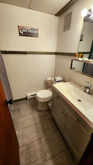 Un bagno con il water, un lavandino, un armadietto e un cartello appeso al muro.