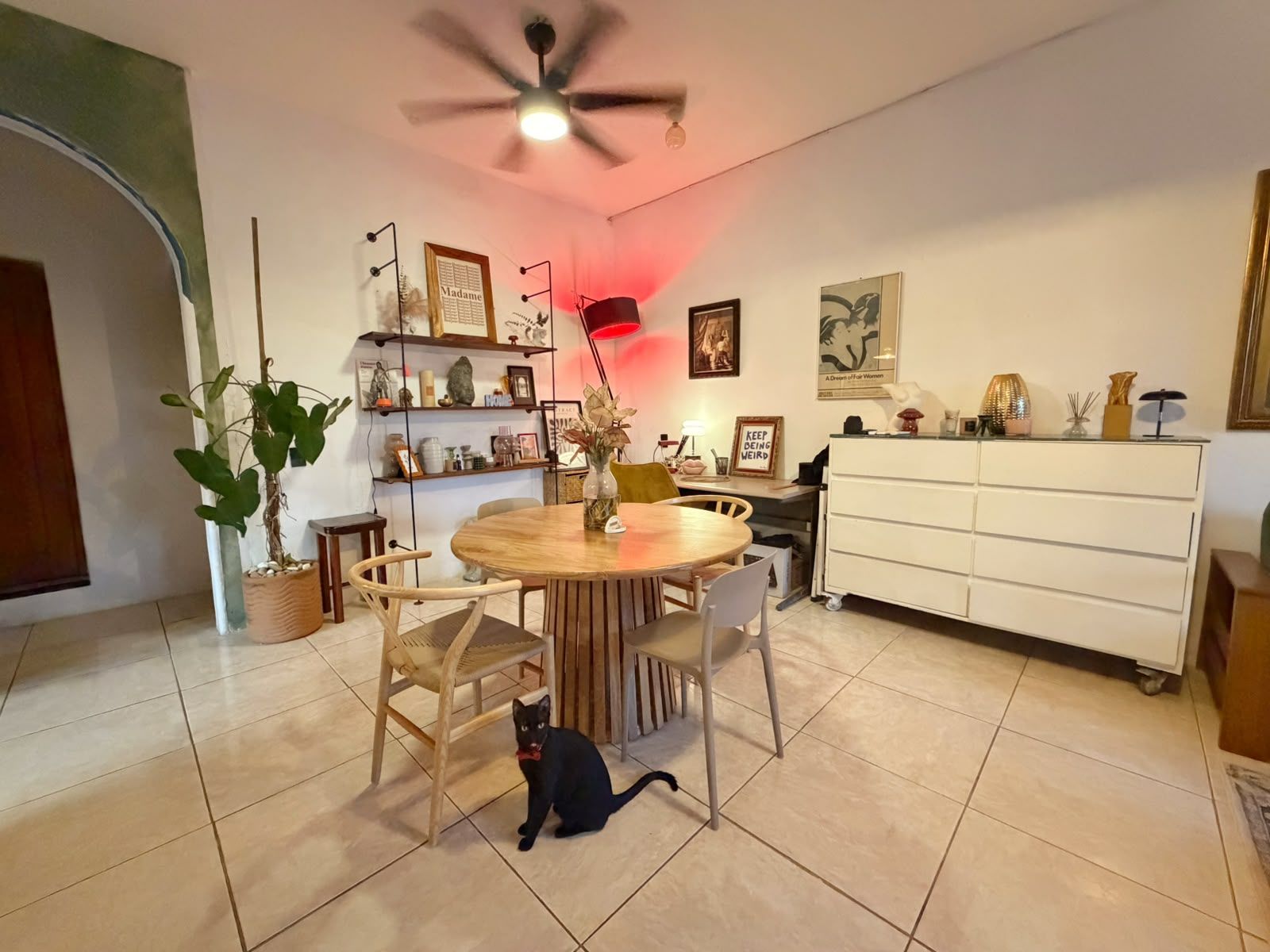 A dining area with a round table, chairs, a ceiling fan, and a white cabinet.