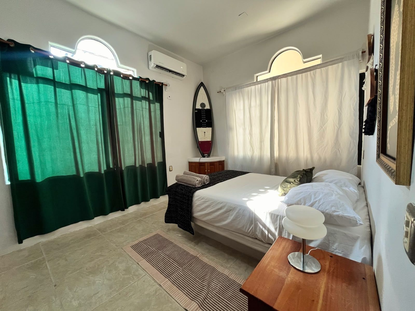 A bedroom with a bed, a bedside table, a mirror, and a window with curtains.