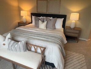 Une chambre à coucher bien rangée, avec un lit, deux tables de chevet, un banc et des œuvres d’art accrochées au mur.