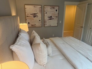 Une chambre à coucher avec un lit, des oreillers, une lampe et des œuvres d’art abstraites accrochées au mur.