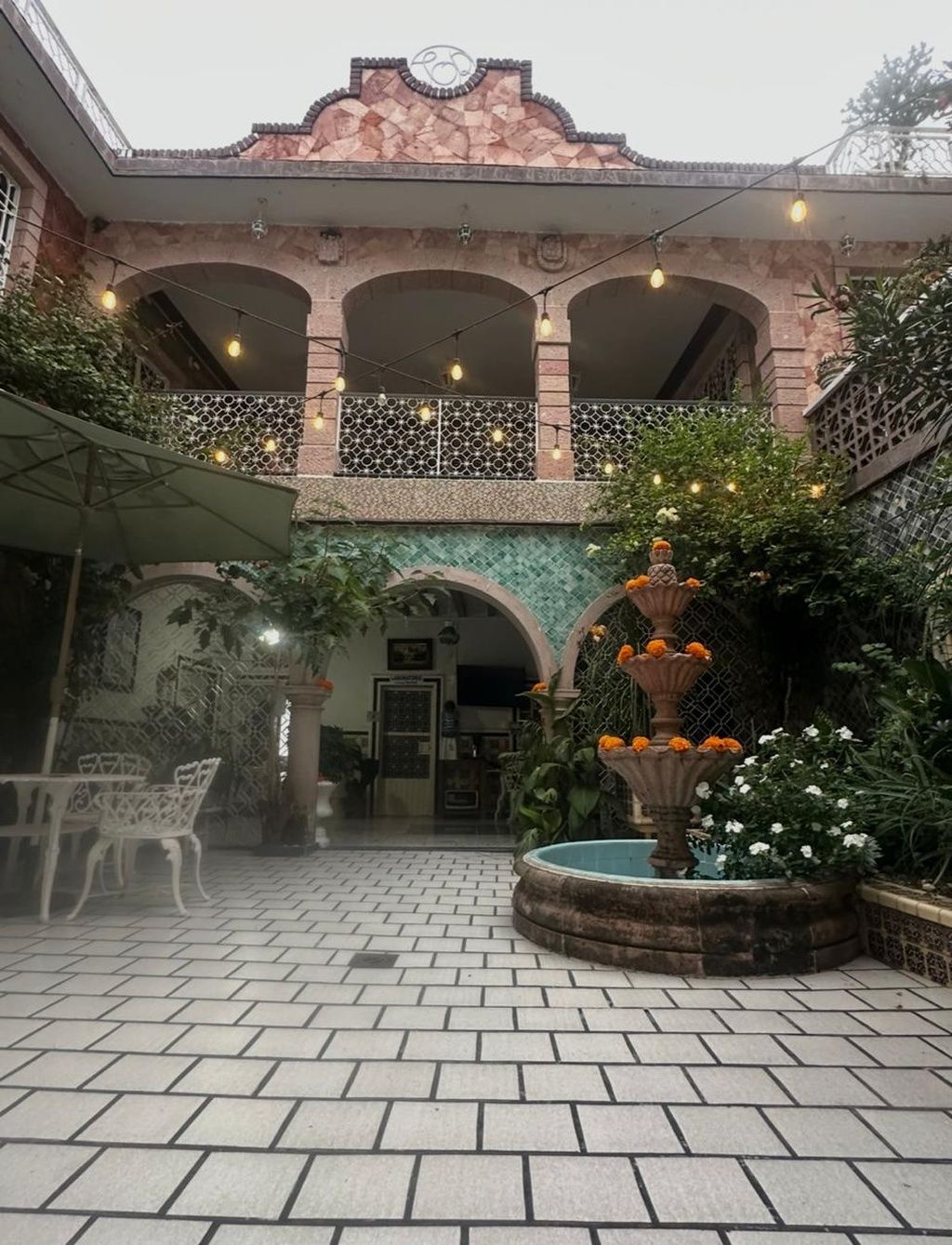 Ein Innenhof mit einem Brunnen, Außenplätzen und einem Gebäude mit einem Ziegeldach und Bögen.