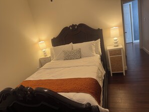 Un letto rifatto con lenzuola bianche e una coperta marrone, affiancato da due lampade da comodino su poggiatesta bianchi.
