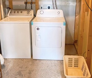 A laundry area with two washing machines and a plastic laundry basket.