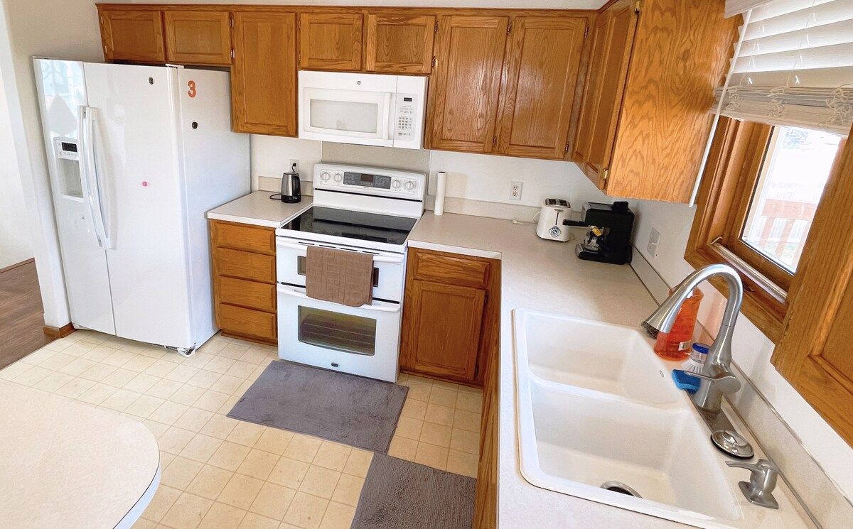 A compact kitchen with wooden cabinets, a white refrigerator, a microwave, an oven, and a sink.
