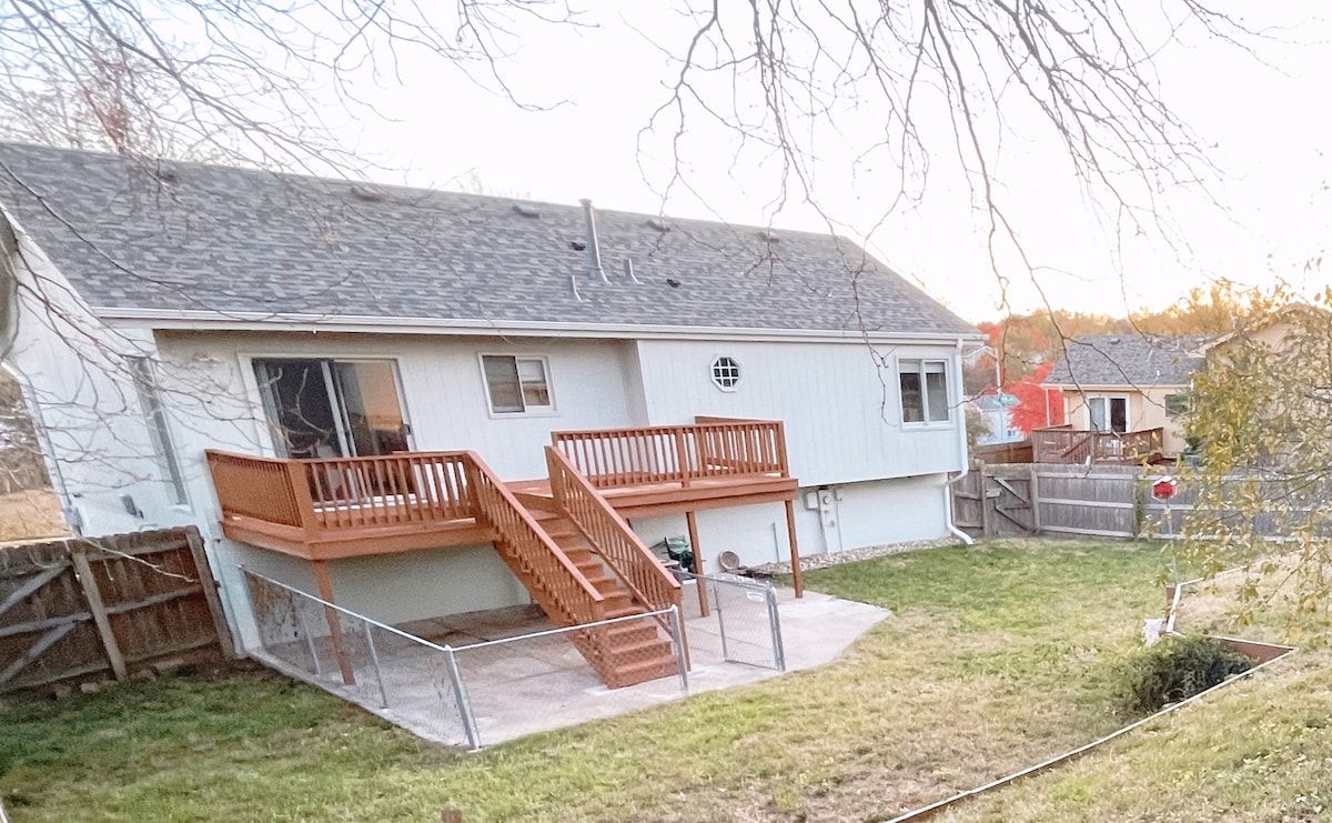 A two-story house with a wooden deck and a staircase leading to a balcony.