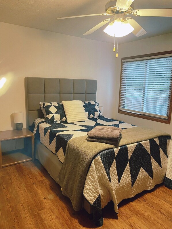 A bedroom with a bed, a nightstand, a ceiling fan, and a window with blinds.