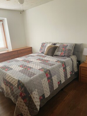 Une chambre à coucher avec un lit, une table de chevet, une lampe et une fenêtre avec des stores.