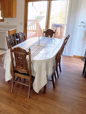 A dining area with a large table, wooden chairs, and a view through a glass door.