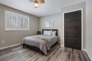 A bedroom with a bed, a ceiling fan, a window with blinds, and a dark door. - Up North Living - Fully furnished updated condo for extended stays in NW WI. (Cumberland)