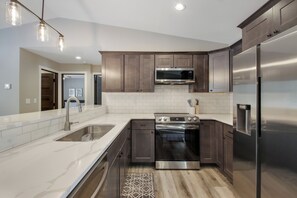 A modern kitchen with stainless steel appliances, dark wooden cabinets, and a white tile backsplash. - Up North Living - Fully furnished updated condo for extended stays in NW WI. (Cumberland)