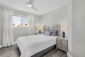 Ein Schlafzimmer mit einem Bett, zwei Nachttischen mit Lampen, einem Deckenventilator und einem Fenster mit Vorhängen.
