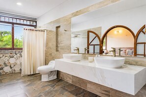 Une salle de bain moderne avec deux lavabos, des toilettes et un grand miroir au design arqué.