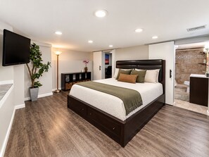 Ein modernes Schlafzimmer mit einem großen Bett, einem Fernseher, einer Pflanze und einem begehbaren Kleiderschrank.