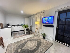 Un saló modern amb zona de cuina, televisió penjada a la paret i una catifa amb dibuixos.