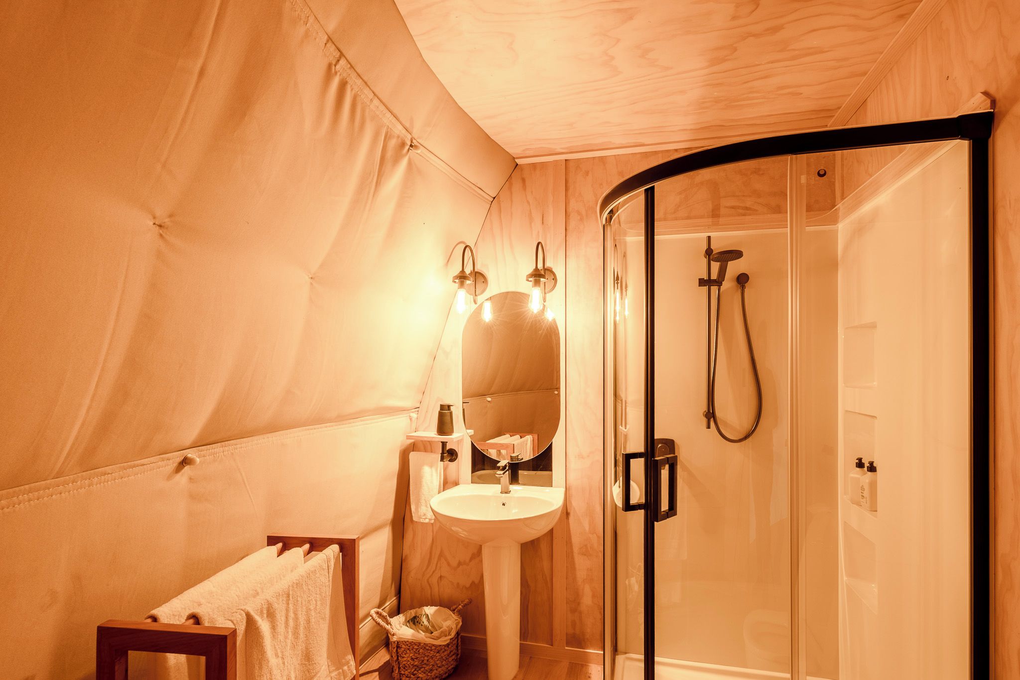 Habitación con carpa, cabina de ducha de vidrio, lavamanos y espejo con luces.