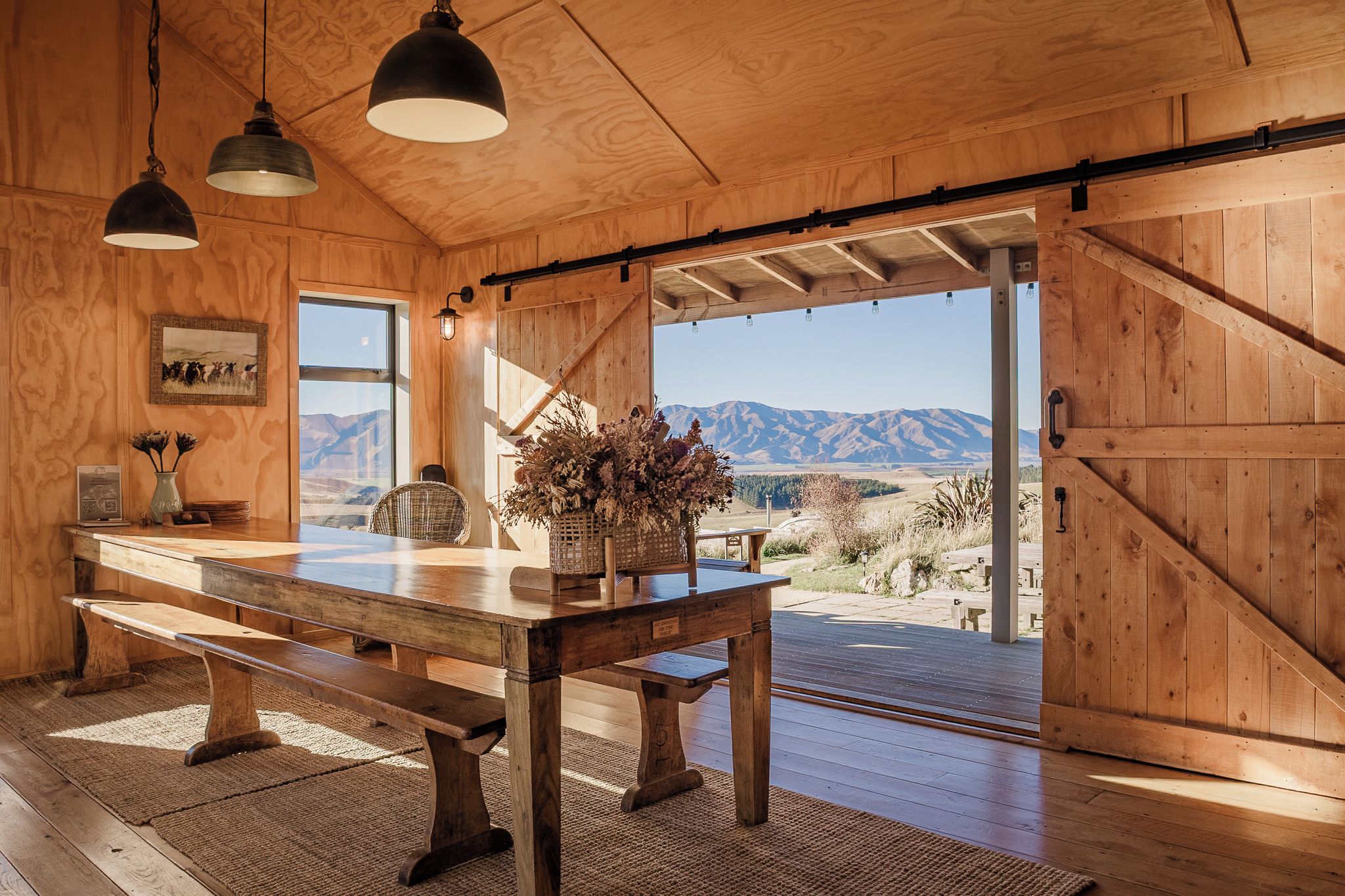 Un interior de madera con una mesa de comedor, bancos, luces colgantes y vistas a las montañas.