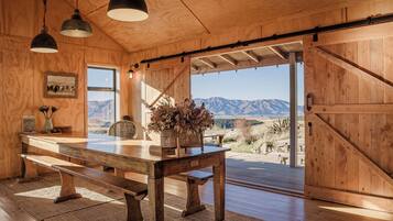 Un interior de madera con una mesa de comedor, bancos, luces colgantes y vistas a las montañas.