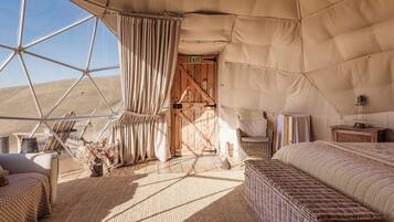 Habitación con carpa, una cama, una silla, una mesita y vista al desierto.