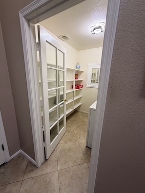 Un couloir avec une porte blanche donnant sur un placard doté de portes et d’étagères en verre.