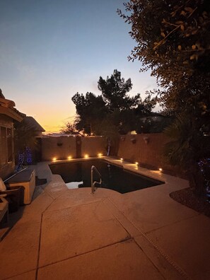 Une piscine entourée d’une terrasse, avec un robinet et des guirlandes lumineuses.