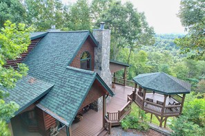 A cabin with a stone chimney, a wooden deck, and a gazebo overlooking a forested area. - Luxury Blue Ridge Retreat, Panoramic Layered Mountain Views & Hot Tub (Morganton)
