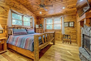 A wooden cabin bedroom with a bed, a ceiling fan, and a stone fireplace. - Luxury Blue Ridge Retreat, Panoramic Layered Mountain Views & Hot Tub (Morganton)