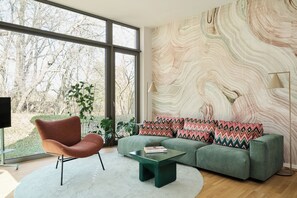 A modern living room with a large window, a green sofa, a round chair, and a marble-patterned wall. - New Listing (Fulda)