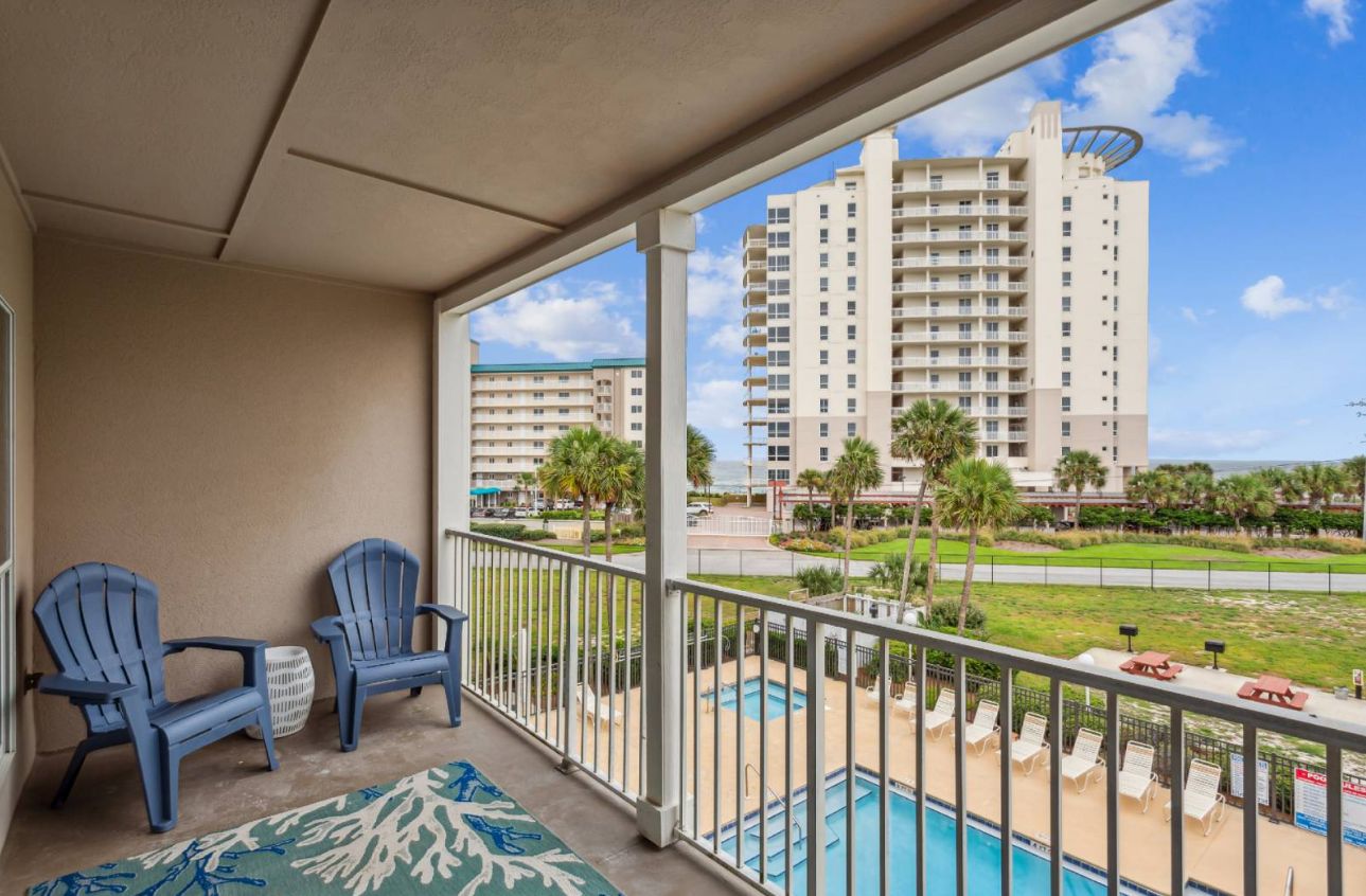 A balcony with two chairs, a pool, and a view of a tall building.