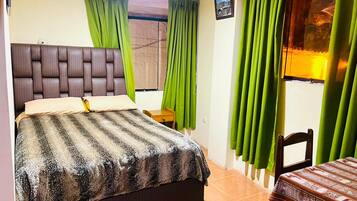 A bedroom with a bed, a nightstand, a chair, and a window with curtains.