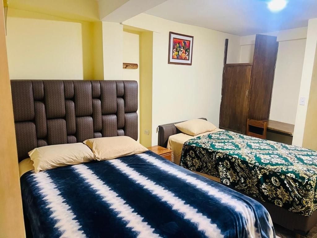 A room with two beds, one with a headboard and the other with a plain headboard. There is a small table and a chair in the room.
