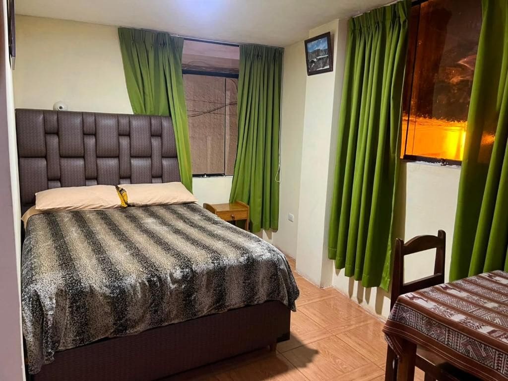 A bedroom with a bed, a bedside table, a chair, and curtains.