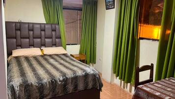 A bedroom with a bed, a bedside table, a chair, and curtains.