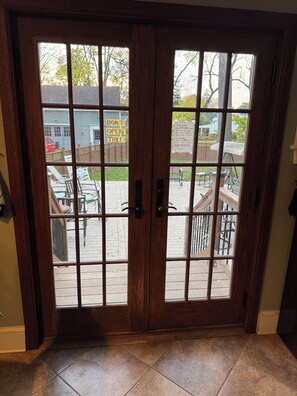 A wooden double door with a grid pattern, leading to an outdoor patio area with a wooden deck, chairs, and a covered table. - Spacious 4-bedroom house in Brighton-Rochester close to everything-dog friendly (Brighton)