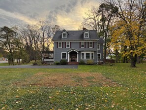 A two-story house with a front porch, a driveway, and a lawn with scattered leaves. - Spacious 4-bedroom house in Brighton-Rochester close to everything-dog friendly (Brighton)