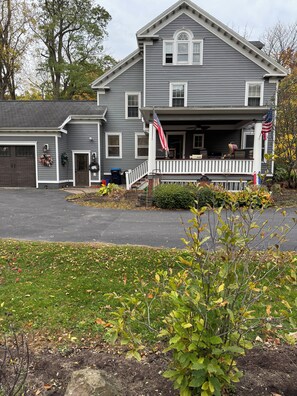 A two-story house with a front porch, garage, and a flag. - Spacious 4-bedroom house in Brighton-Rochester close to everything-dog friendly (Brighton)