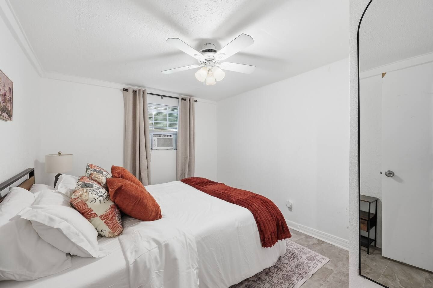 Een slaapkamer met een bed, een plafondventilator, een raam met gordijnen en een deur.