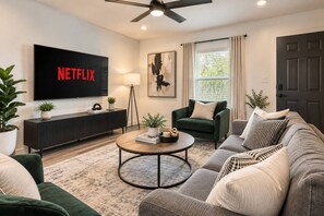 Een moderne woonkamer met een flatscreen televisie, een bank, een salontafel en een vloerlamp.
