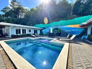 Une piscine dotée d’une terrasse carrelée, de chaises longues et d’un espace couvert orné d’une fresque murale.