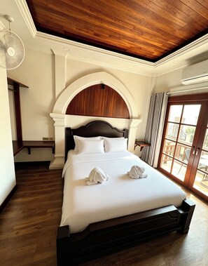 Une chambre d’hôtel avec un grand lit, un plafond en bois et une vue sur l’extérieur, visible à travers une porte vitrée.