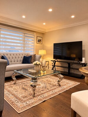 Un salon comprenant un canapé, une table basse en verre, un tapis, un téléviseur et une lampe.
