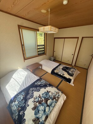 Ein Zimmer mit zwei Betten, einem Fenster, einem Deckenventilator und einer Wandklimaanlage.